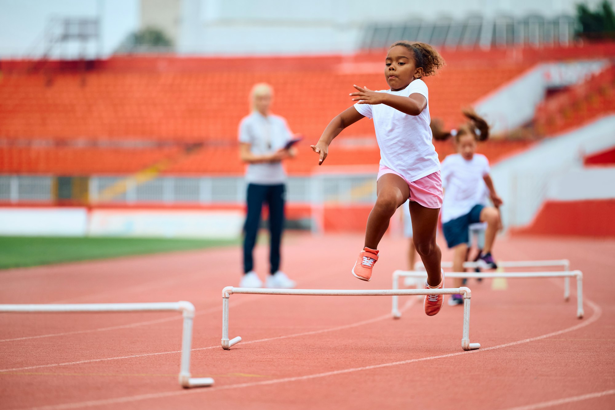 Black girl running on hurdling track at the stadium.