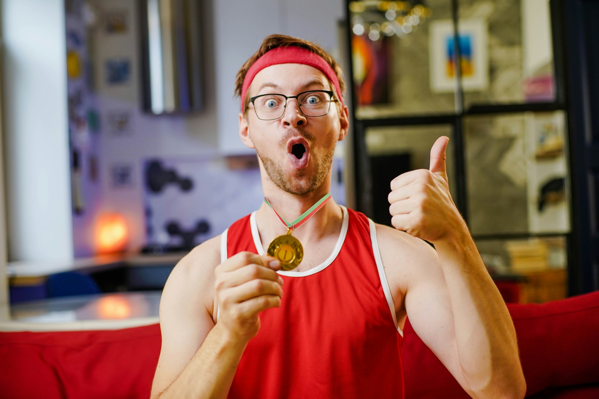 Portrait of funny excited athlete sitting on sofa with gold medal.